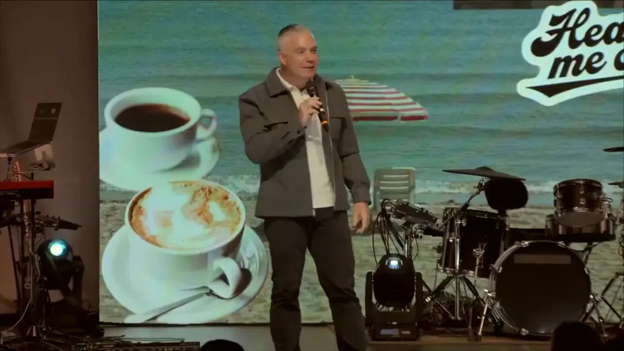 Speaker centered on stage gesturing with one hand while holding a microphone, 'Hear me out' backdrop visible