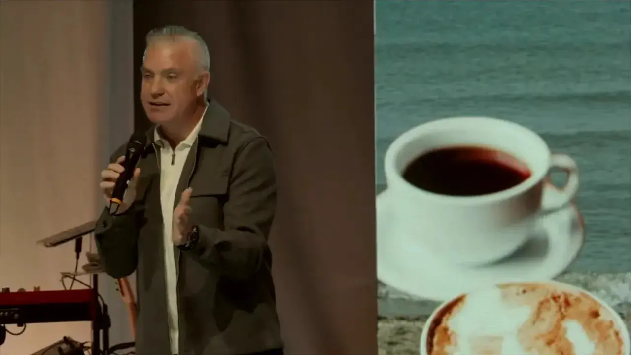Speaker on stage gesturing with arm extended and the 'Hear me out' message partially visible on the backdrop