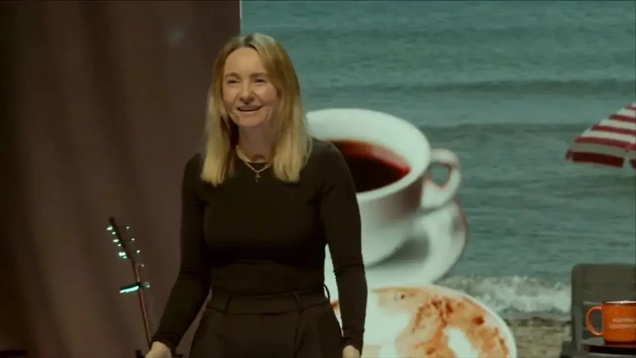 Beach-themed stage with striped umbrella, table with mug and book, and the speaker at right
