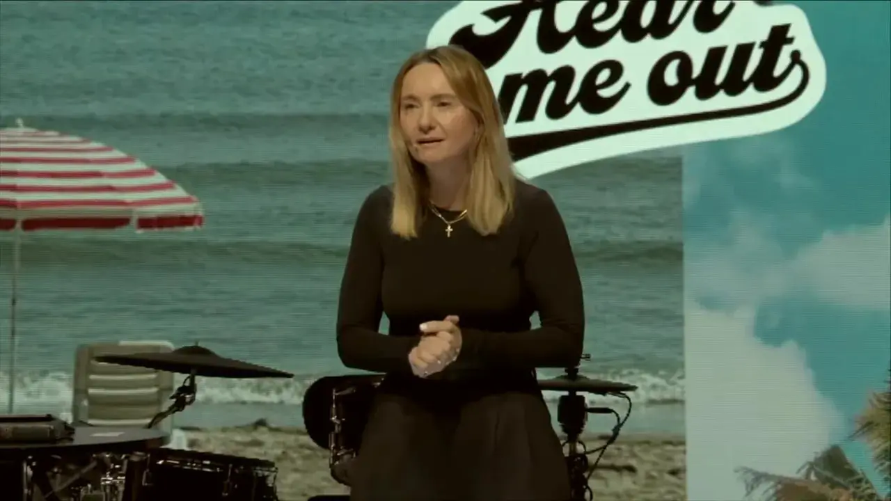 Beach-themed stage with striped umbrella, table with mug and book, and the speaker at right