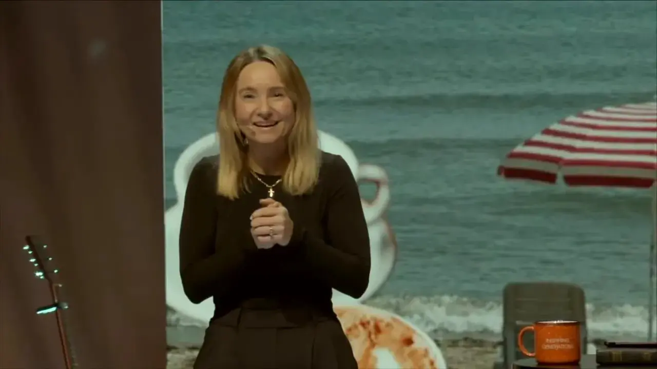 Beach-themed stage with striped umbrella, table with mug and book, and the speaker at right